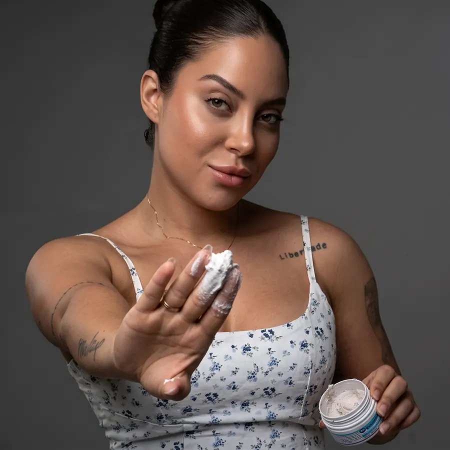 Mulher com o Esfoliante Amazolé na ponta dos dedos, segurando o pote aberto
